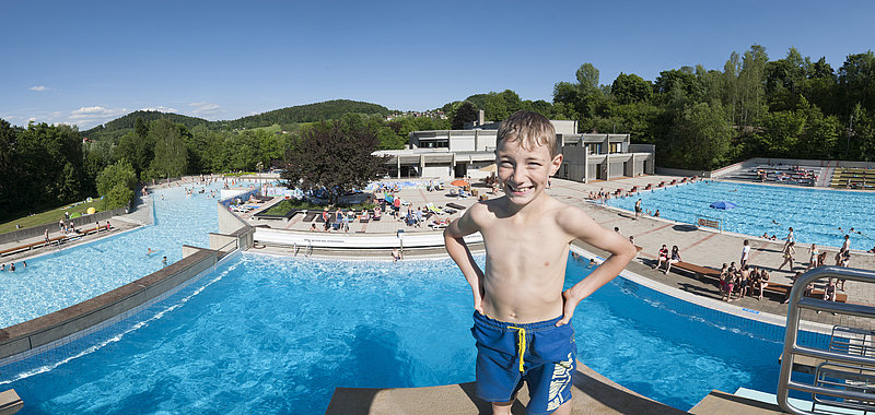 Ein Junge steht auf dem Sprungturm. Im Hintergrund ist ein Panoramablick auf die Wasserflächen zu sehen.